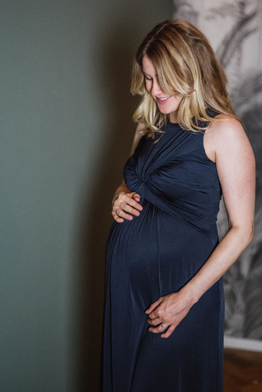 Frau im festlichen Schwangerschaftskleid hält Babybauch