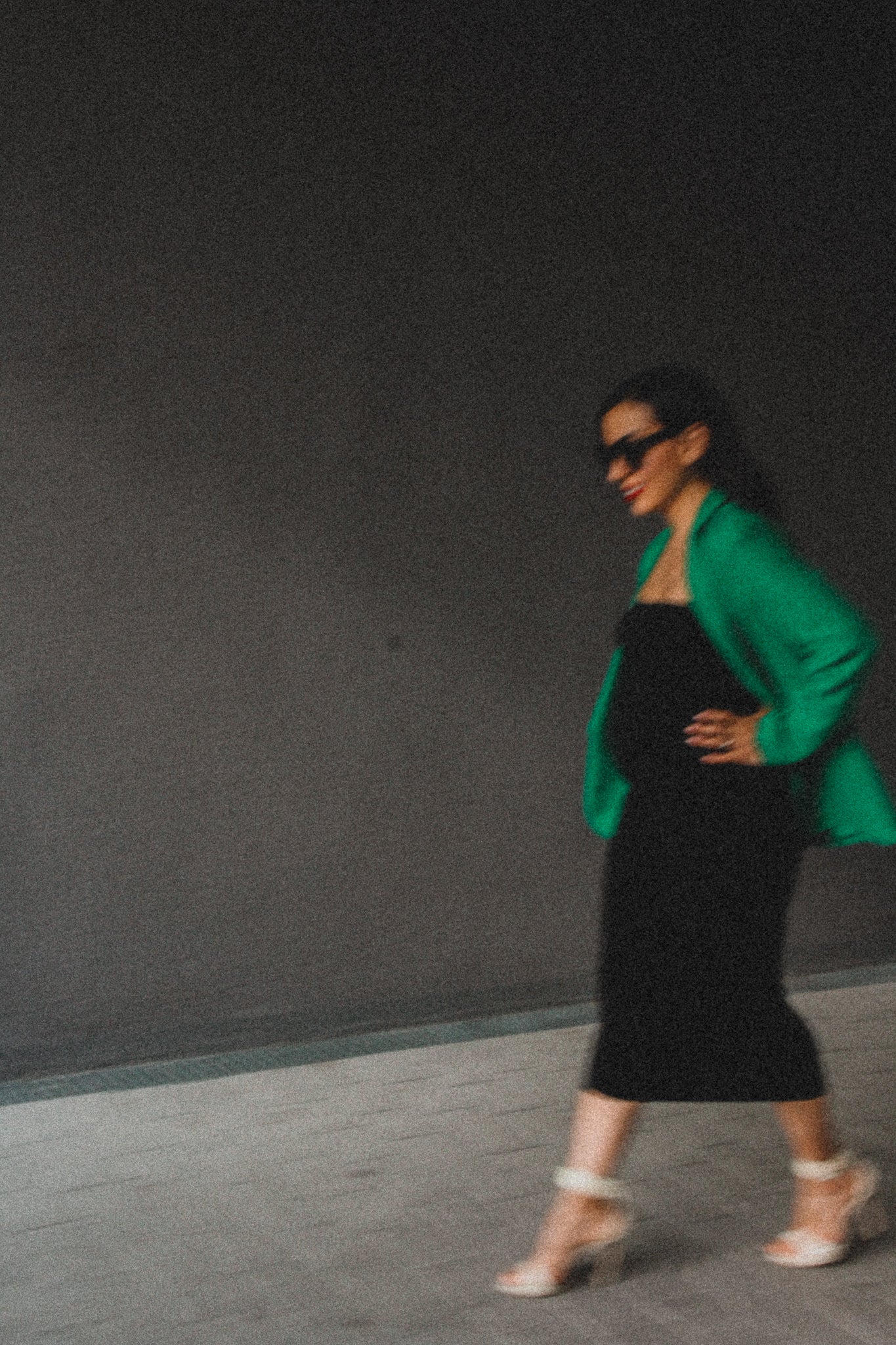 Schwangere Frau mit schwarzem Kleid und grünem Blazer in Bewegung